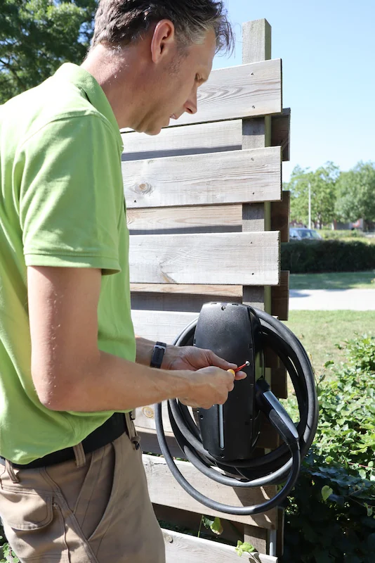 Mark van Gameren monteert een laadpaal aan een houten schutting